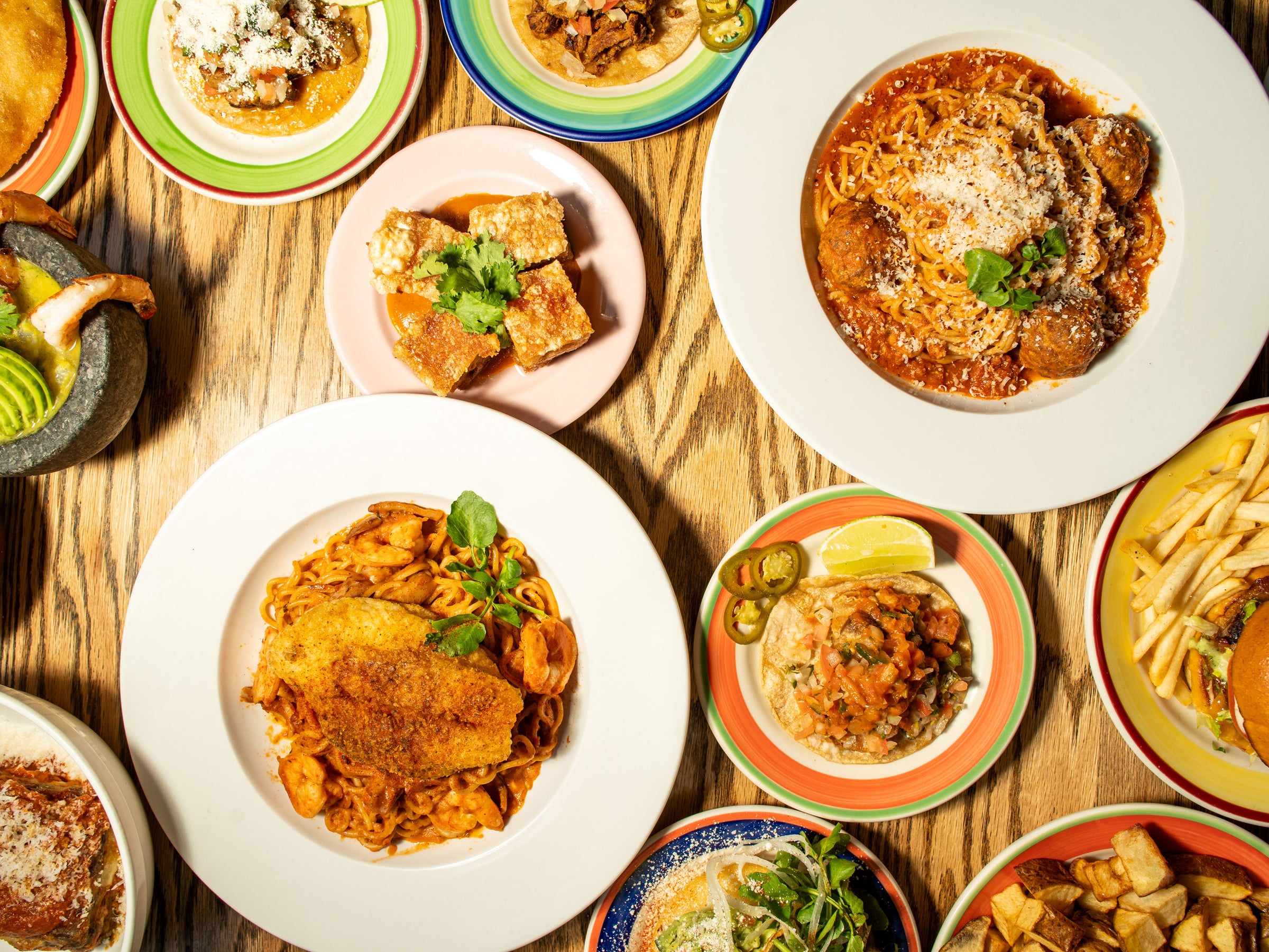 Spread of La Ñapa dishes on a wood table — tacos, chicharrón, pastas, pescado a lo macho and more, Latin Caribbean cooking in Brooklyn